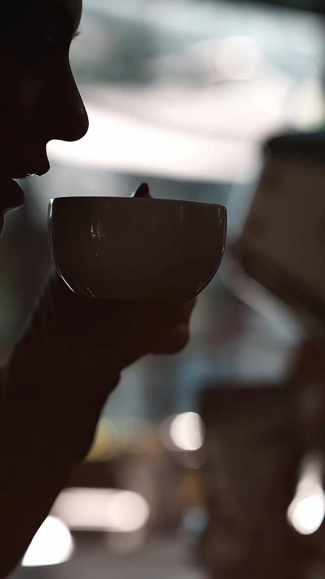 Silhouette in profile bringing a white cup to the lips