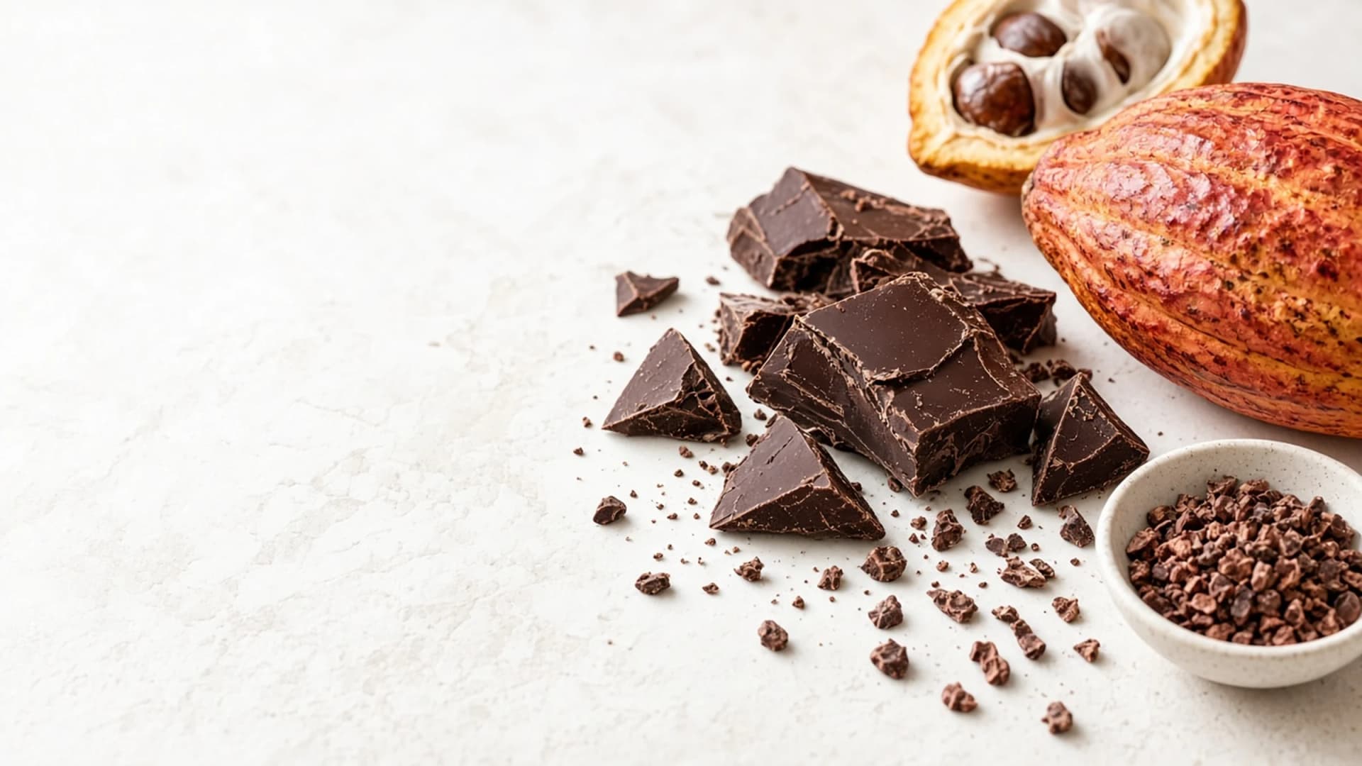 Cacao pod and dark chocolate pieces on ivory stone