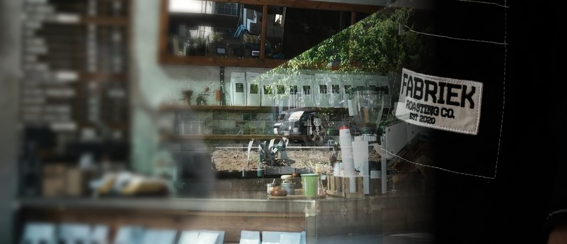 Café counter with coffee bags, and a black FABRIEK Roasting Co. work jacket